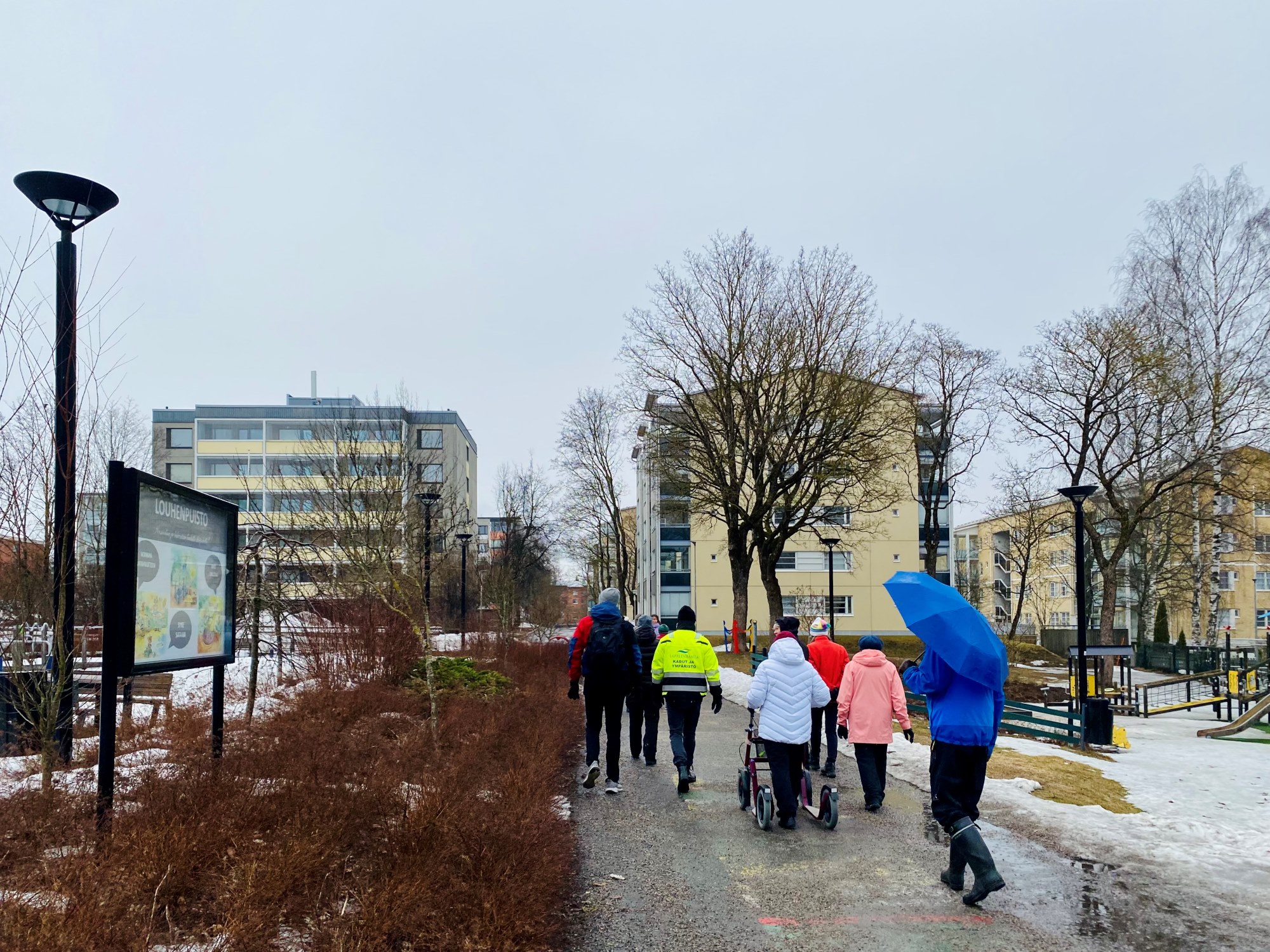 Asukaskävely Peltolassa. Puistoa, puita, ihmisiä, kerrostaloja.